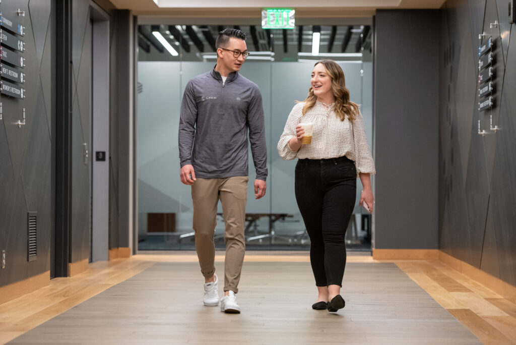 A man and woman dressed in business casual attire walk in a hallway at Turnberry's Minneapolis offices